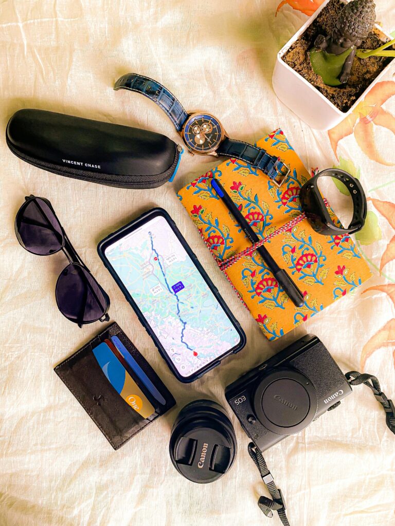 pexels-photo-13002684-13002684 Flat lay of travel essentials including smartphone with map, camera, and sunglasses.